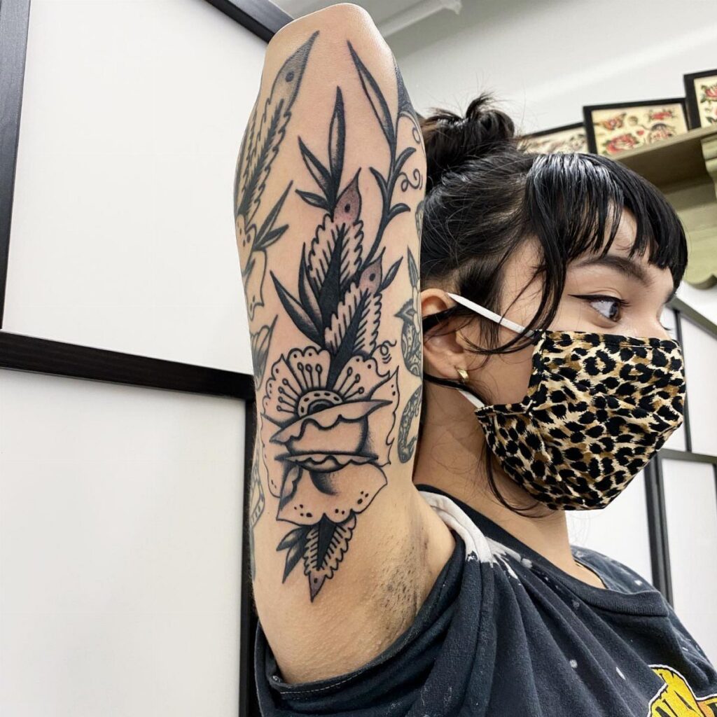 Tattoo of a flower and leaves on the back of a person's arm