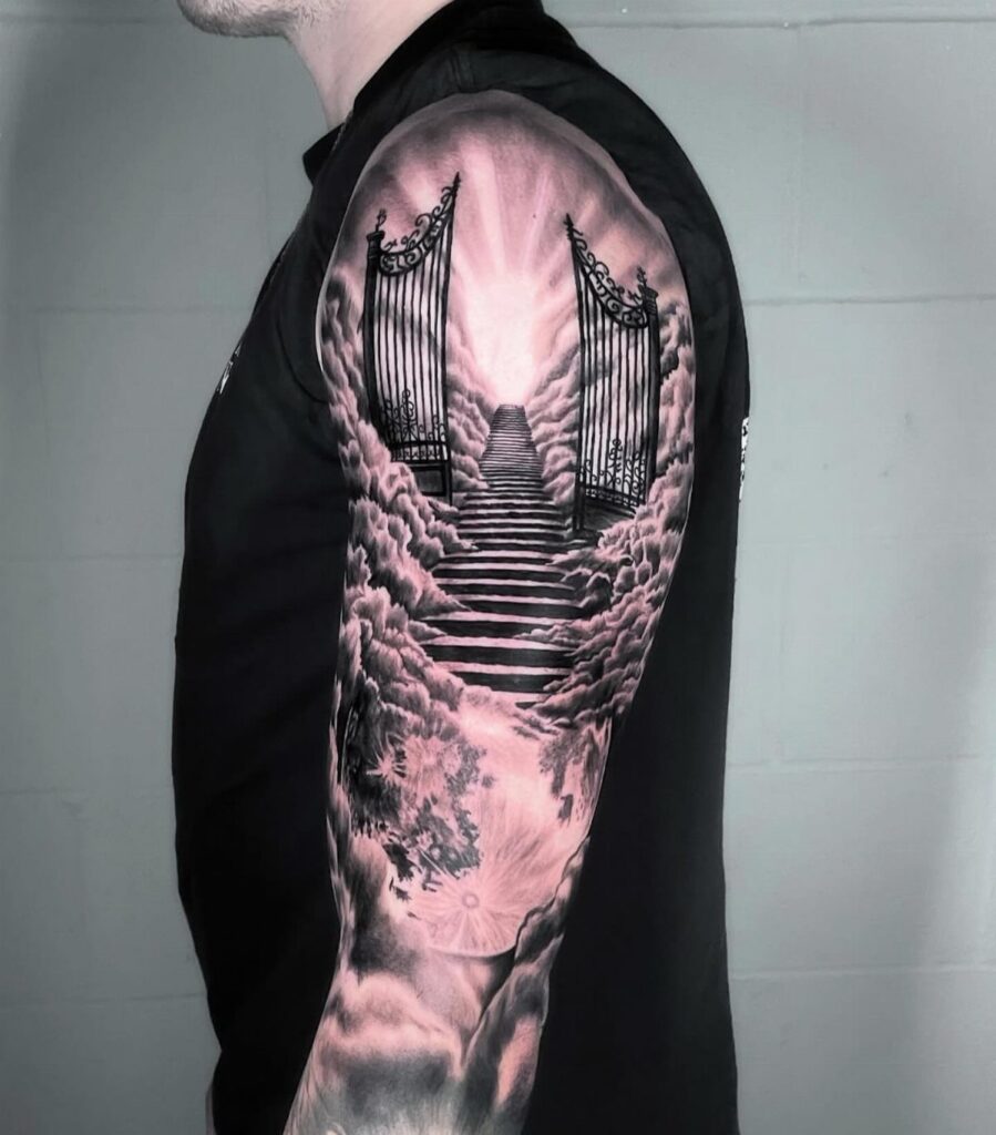 Tattoo on a man's arm showing heavenly gates and stairs among fluffy clouds.