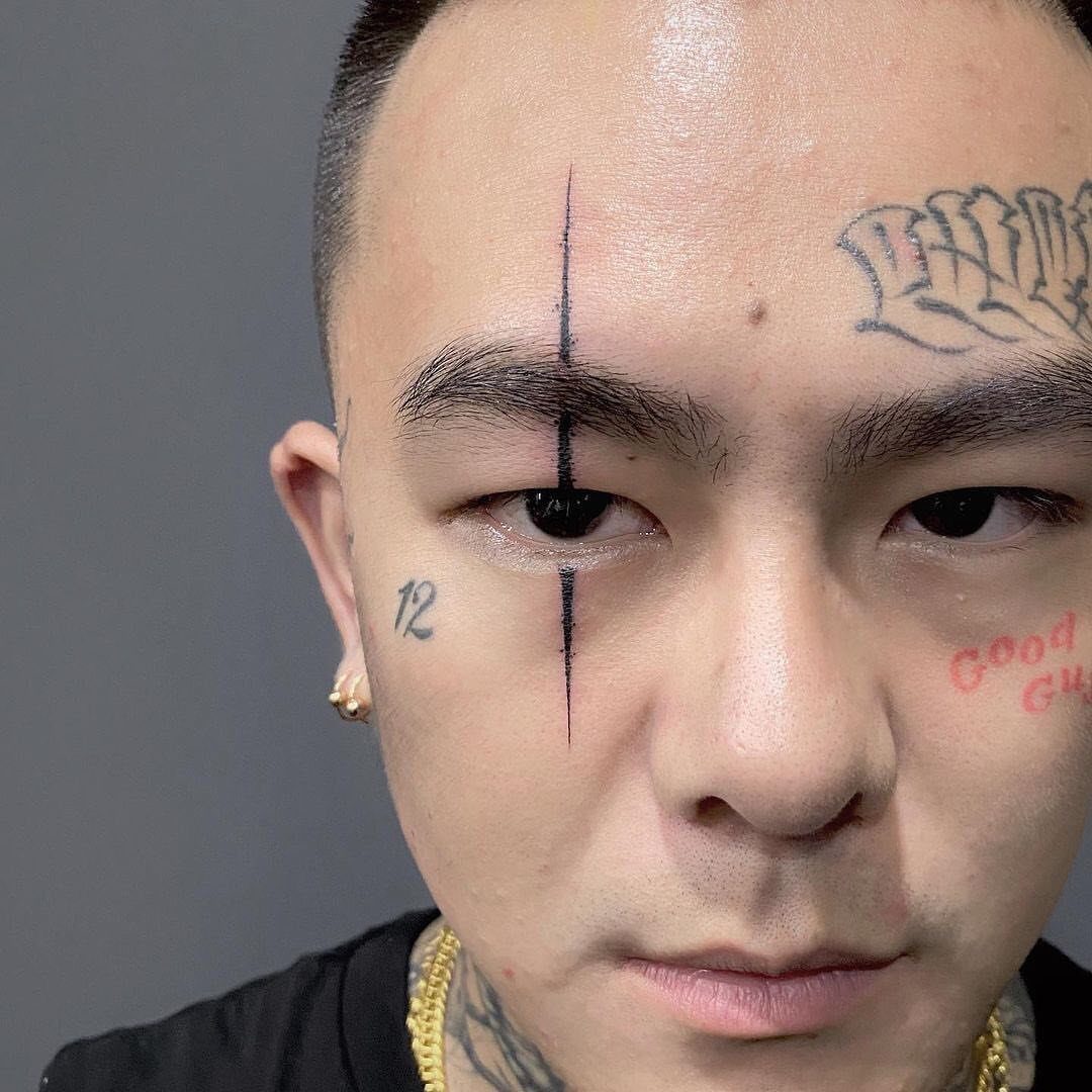 Man with various black ink face tattoos including a vertical line and script.