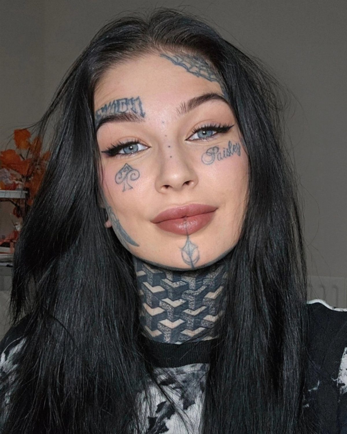 Woman with long black hair and extensive black ink tattoos on her face and neck.
