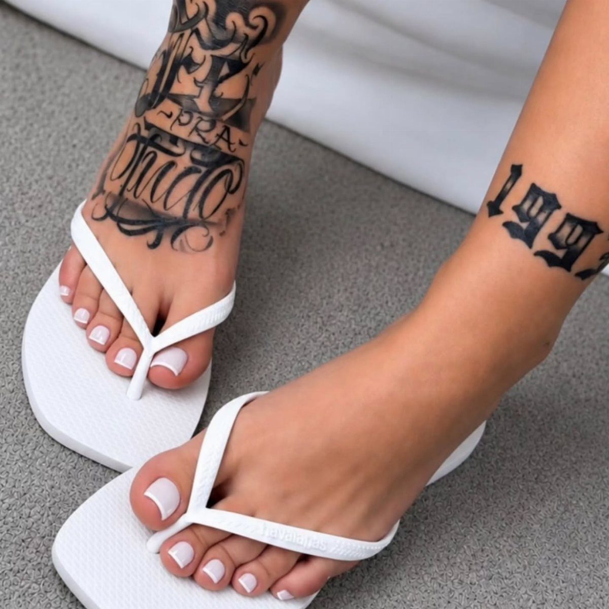 Woman's feet in white flip-flops featuring black ink tattoos on the ankles and feet.