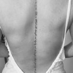 Woman's back with a vertical quote tattoo and cross along the spine.