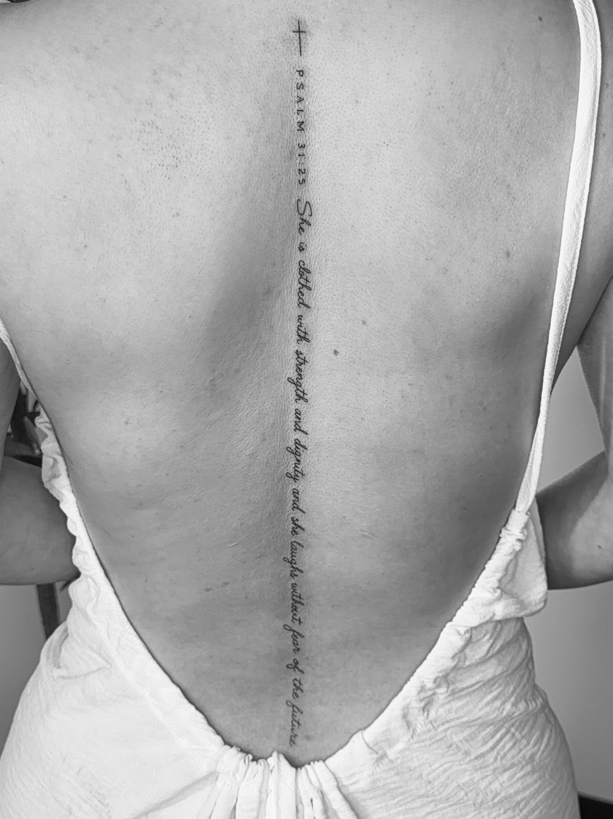 Woman's back with a vertical quote tattoo and cross along the spine.