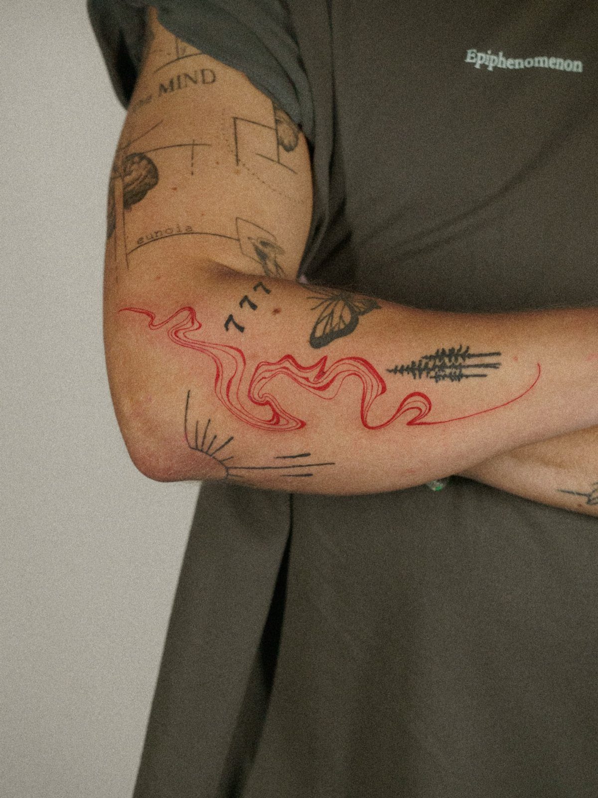 Arm with fine line tattoos including a red wave and black geometric symbols
