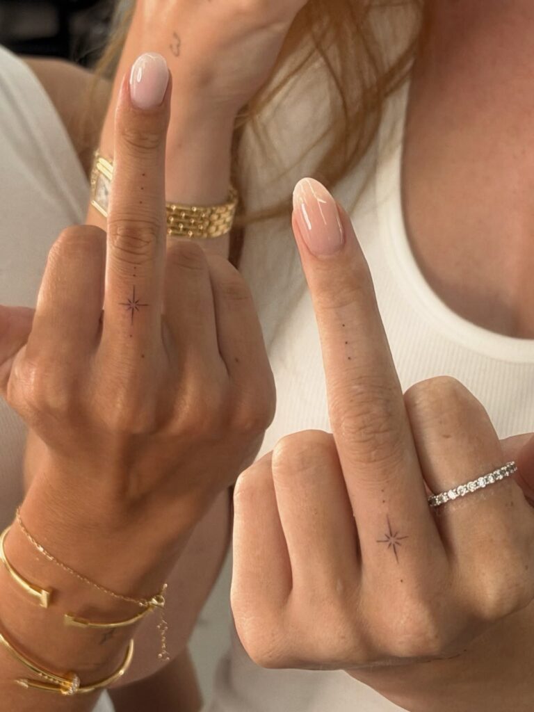 Two hands showing small black star tattoos on the middle fingers.