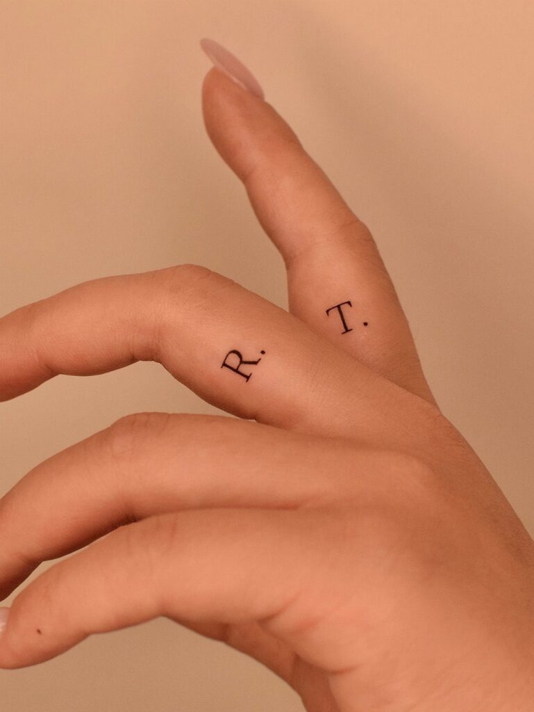 Hand with small black letter tattoos on the index and middle fingers.