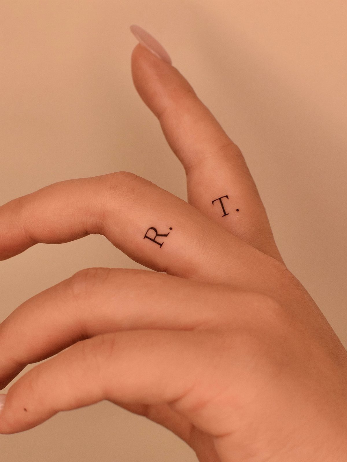 Hand with small black letter tattoos on the index and middle fingers.