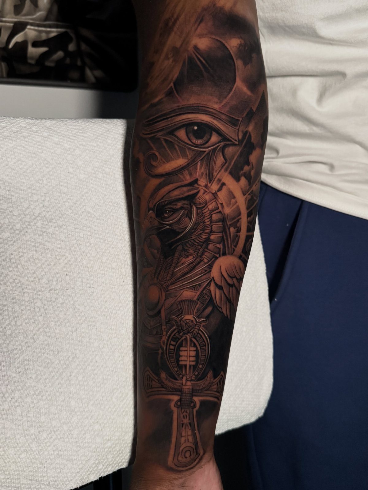 Forearm sleeve tattoo with black and grey Egyptian symbols including the Eye of Horus.