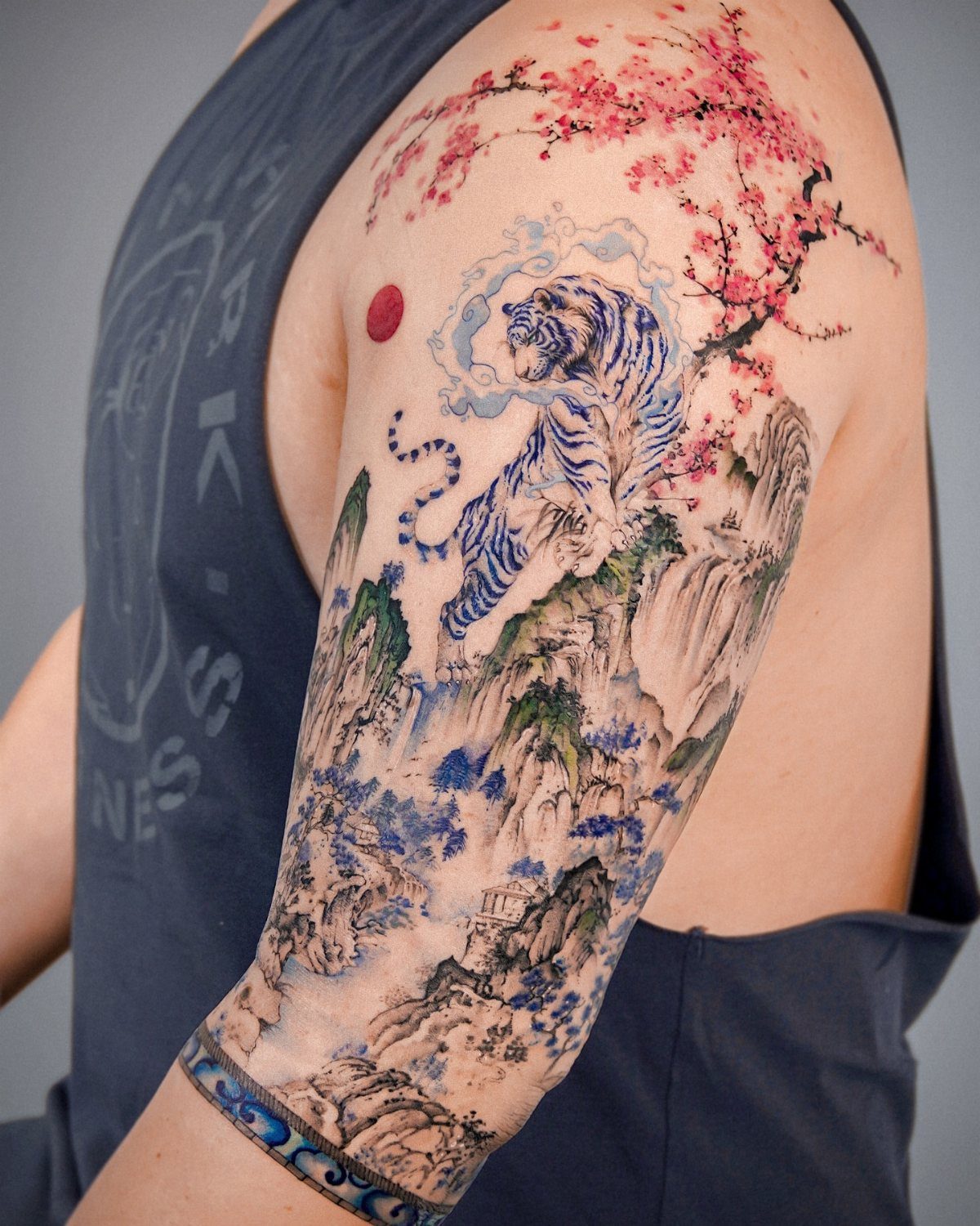 Half sleeve tattoo of a blue tiger and cherry blossoms on an arm