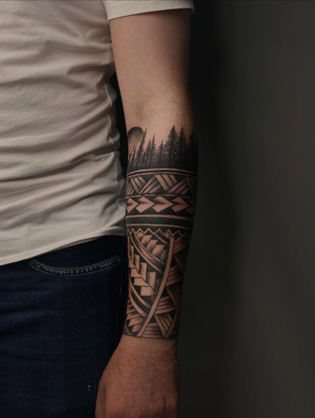 Forearm with a black ink half sleeve tattoo featuring forest and geometric patterns