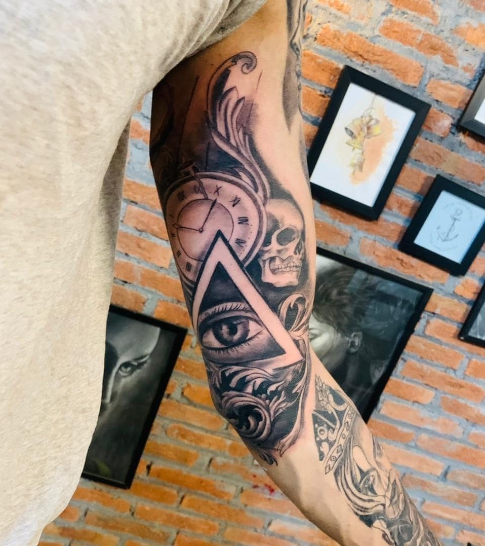 Inner bicep tattoo on a man featuring a clock, skull, and eye design.