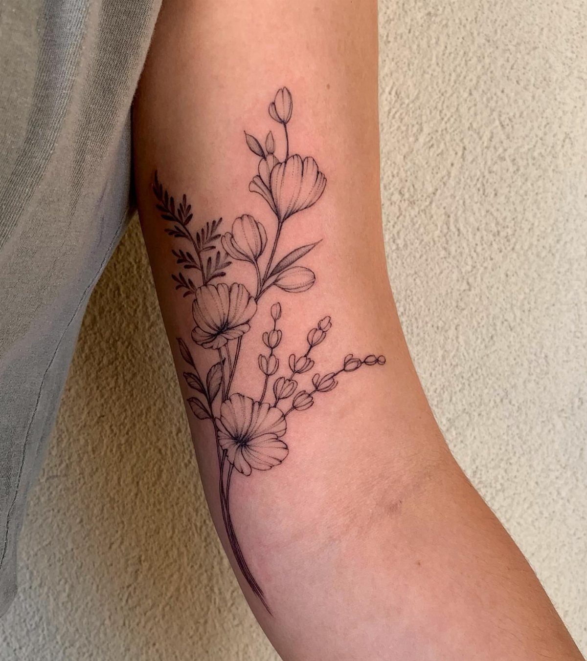 Delicate floral minimalist tattoo on the inner bicep of a person's arm.