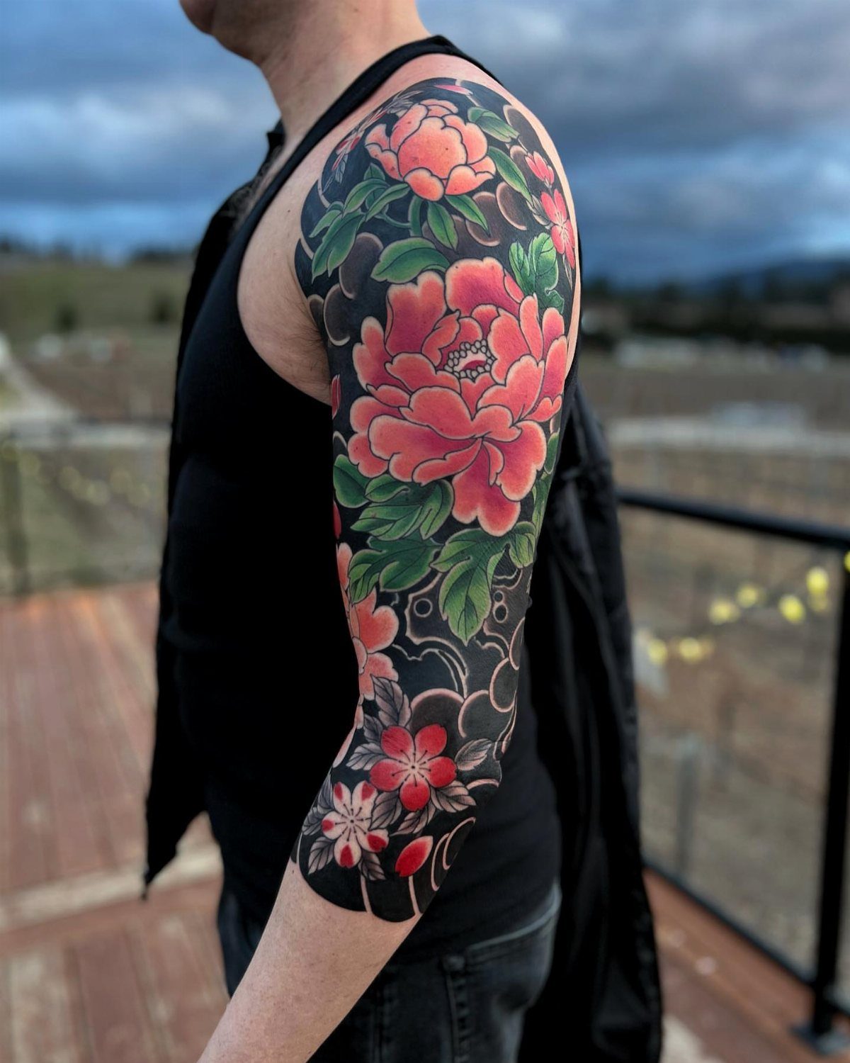 Man's arm with a Japanese tattoo of red peonies and green leaves.