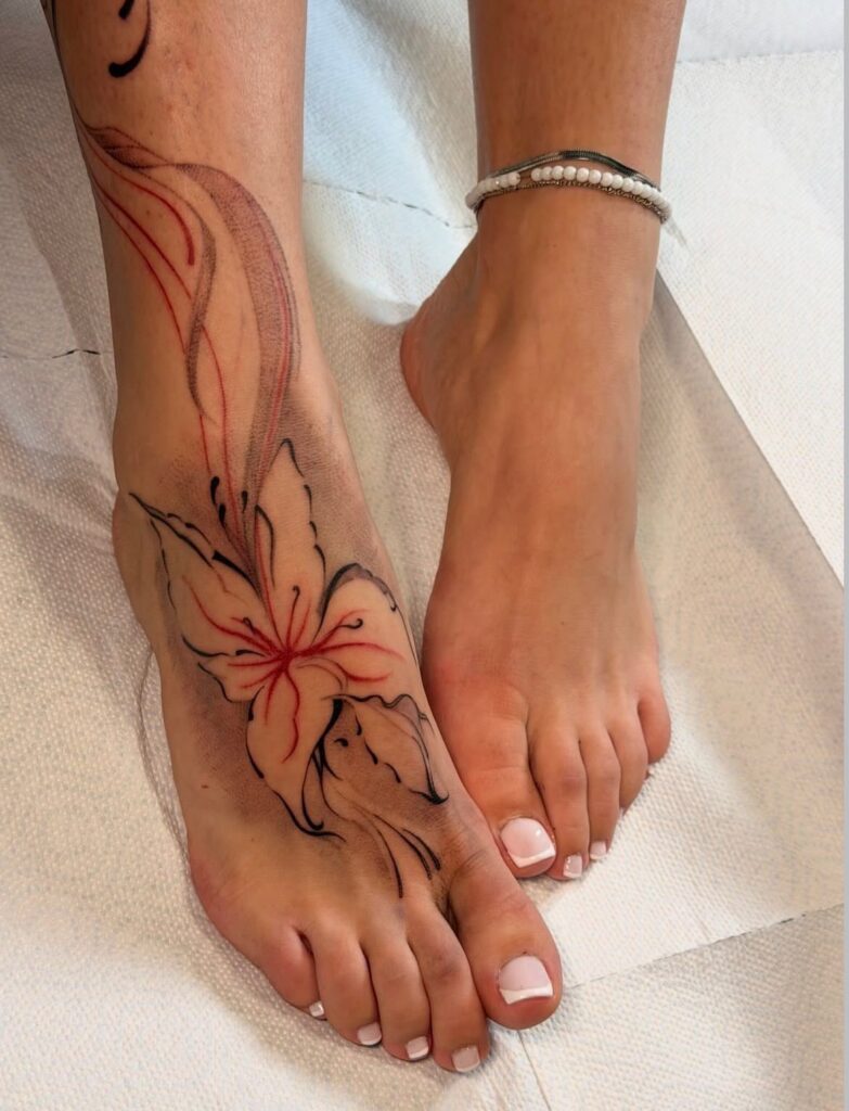 Woman's foot and ankle featuring a red lily tattoo with flowing black lines.