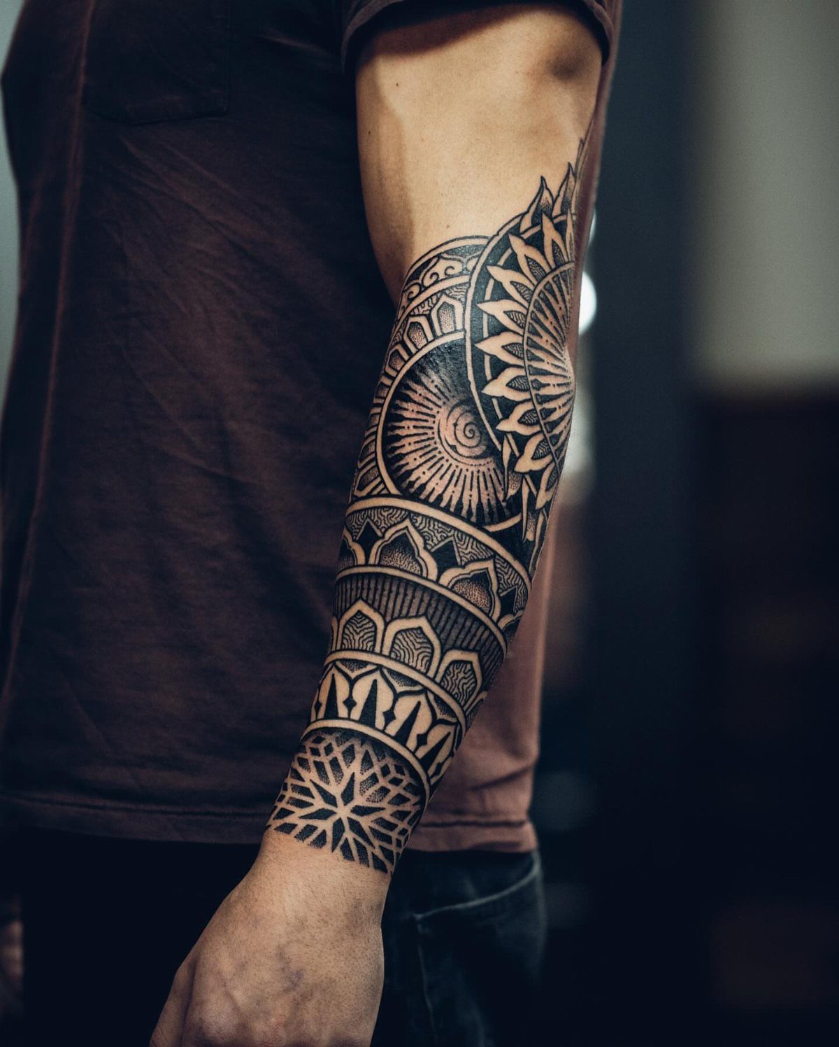 Man's forearm with a detailed black ink geometric mandala tattoo from wrist to elbow
