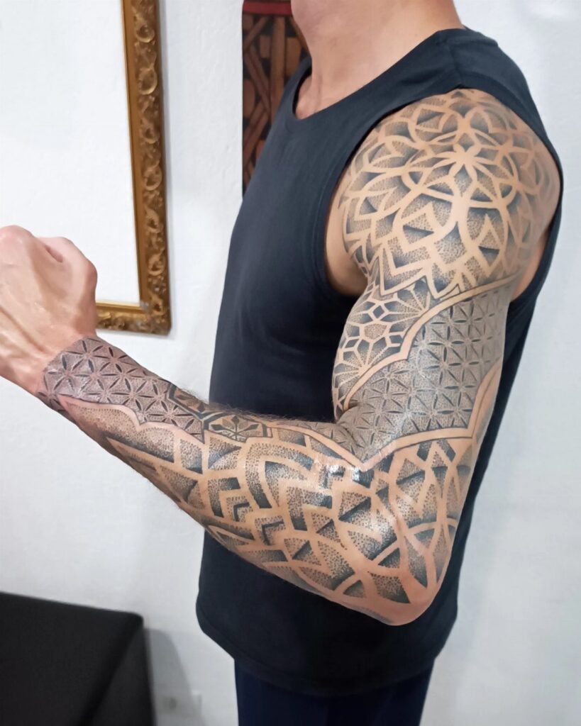 Muscular arm with a detailed geometric mandala sleeve tattoo in black and grey ink.