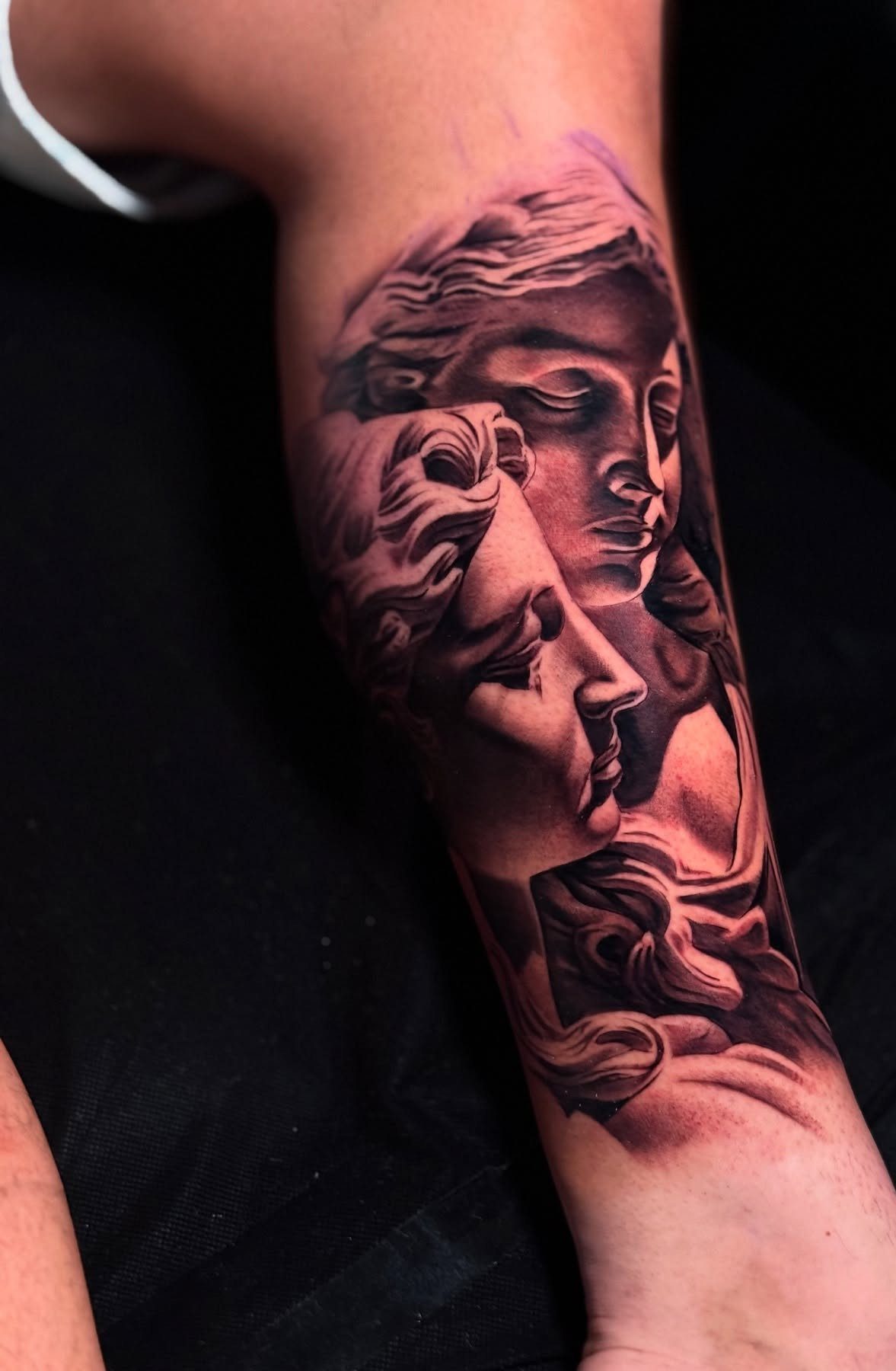 Detailed black and grey realism tattoo of classical faces on a man's leg.