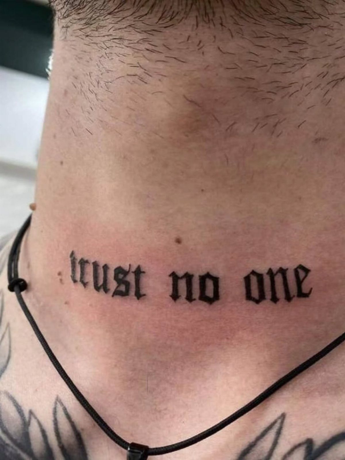 Man's neck with a black gothic tattoo reading trust no one