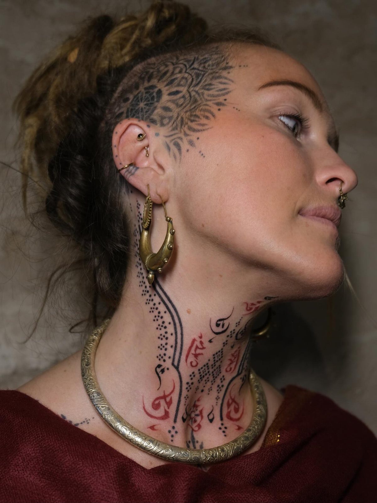 Woman with detailed black and red tattoos on her neck and shaved head.