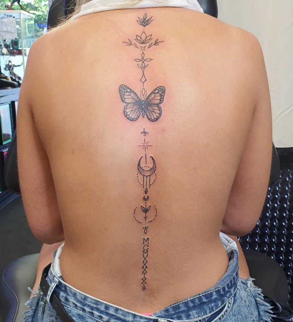 Woman's back with a vertical black ink tattoo featuring a butterfly and moon.