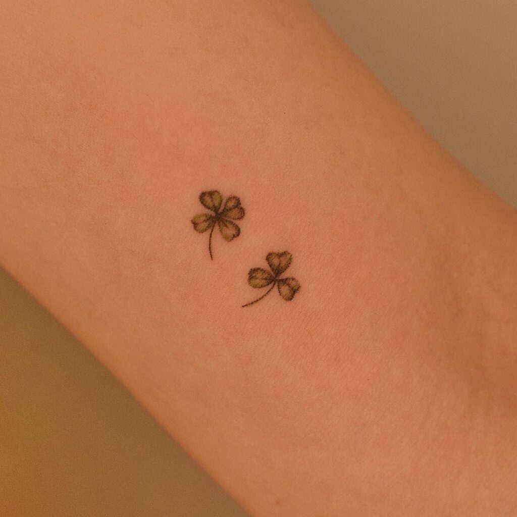 Two small green clover tattoos, one four-leaf and one three-leaf, on an arm.