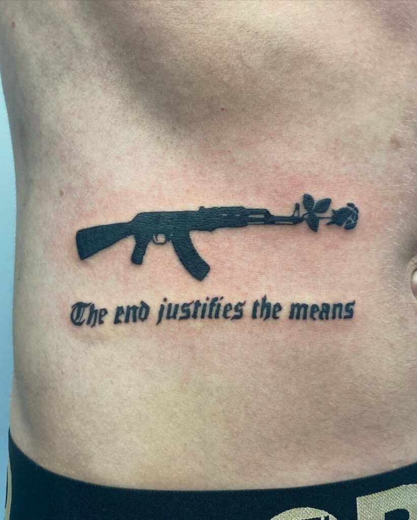 Rib tattoo of an AK-47 rifle with a rose and gothic text on skin.