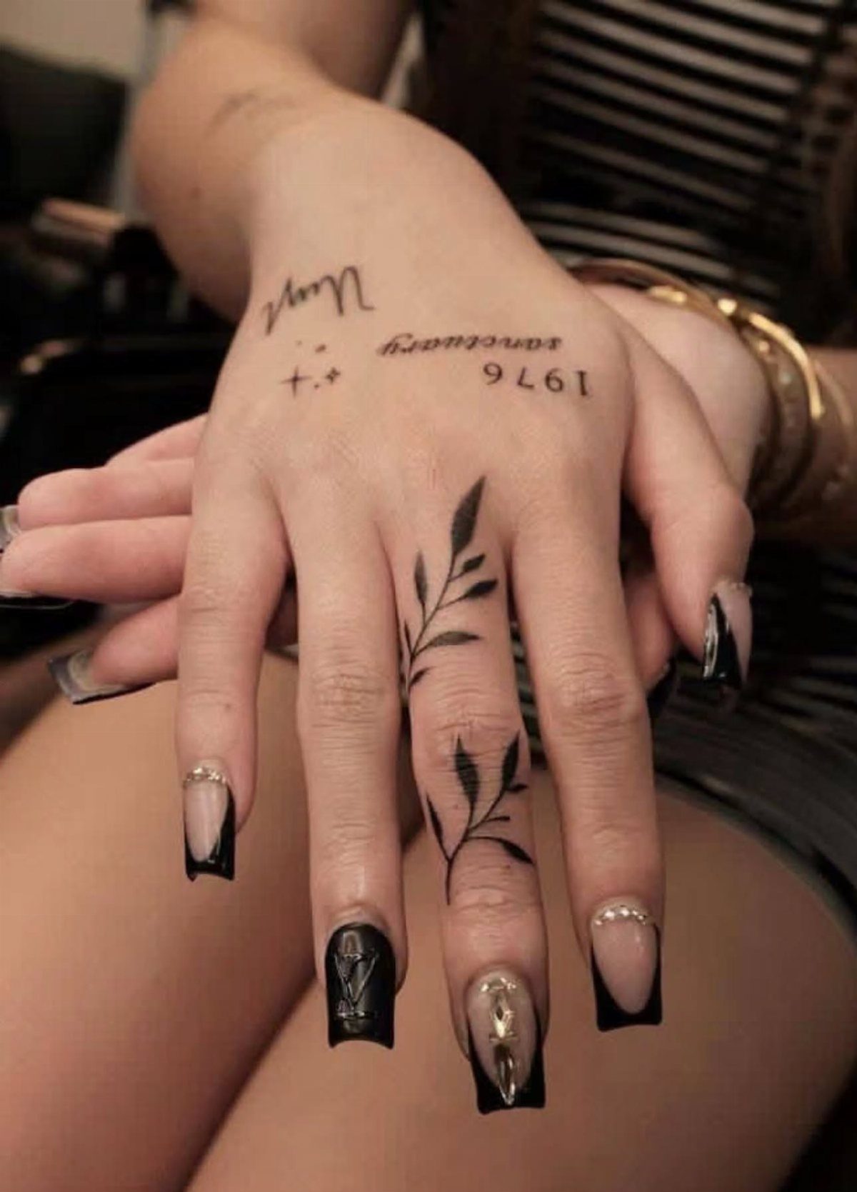 Hand with a leafy branch tattoo on the ring finger and long nails.