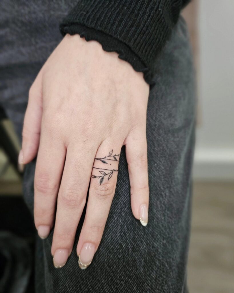Hand with two delicate black leaf ring tattoos circling the ring finger