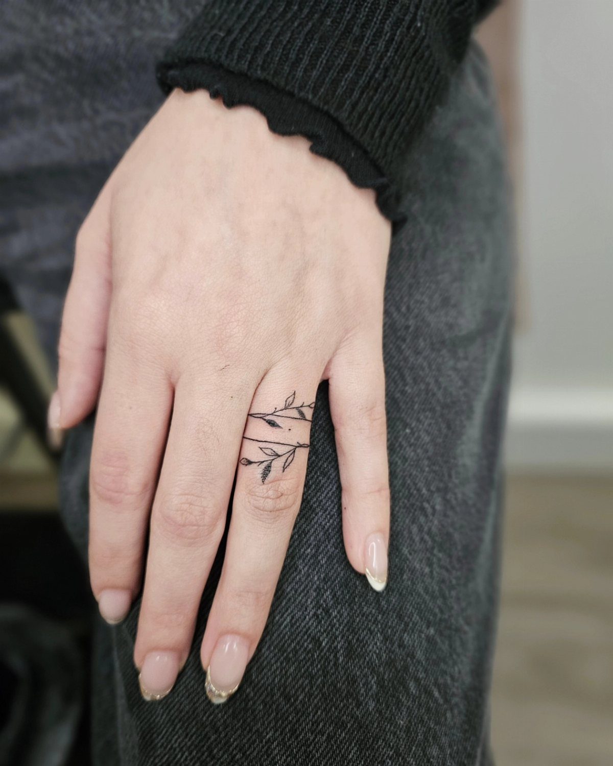 Hand with two delicate black leaf ring tattoos circling the ring finger