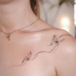 Delicate black ink butterfly tattoo on a woman's shoulder and collarbone area