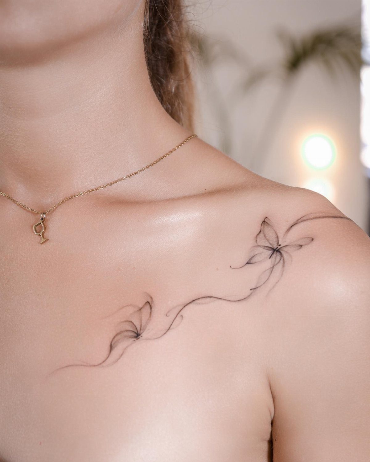 Delicate black ink butterfly tattoo on a woman's shoulder and collarbone area