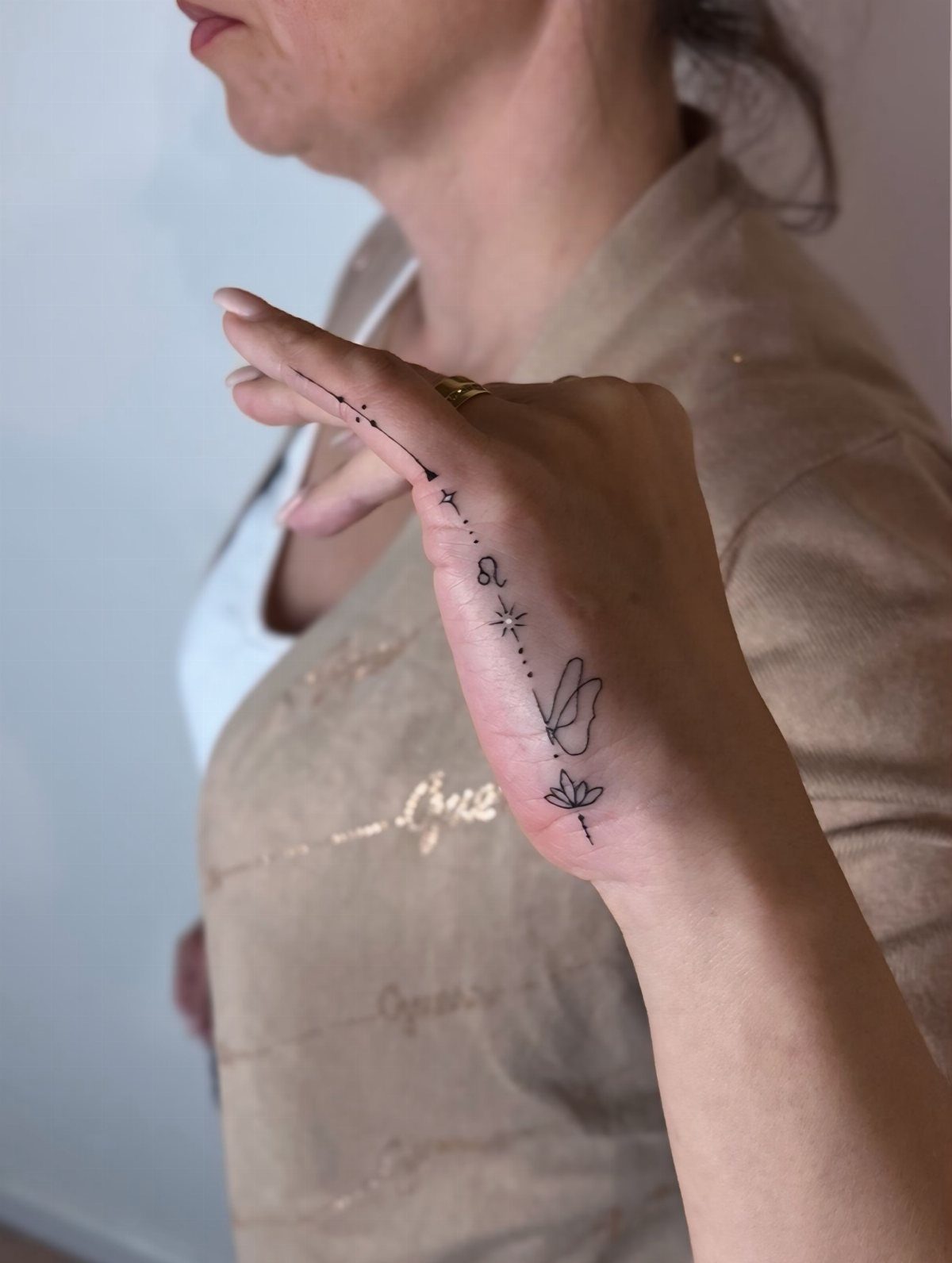 Hand with a delicate fine-line tattoo of stars and symbols on the side.