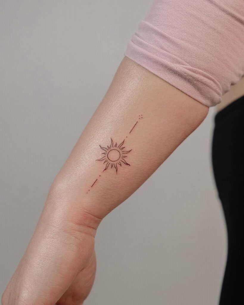 Small sun tattoo with fine lines and dots on a person's inner forearm.