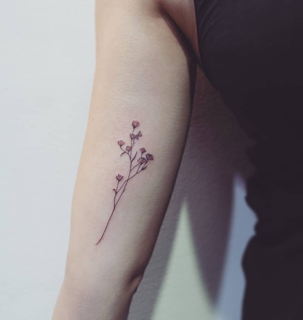 Small floral tattoo with pink blossoms on a person's inner upper arm