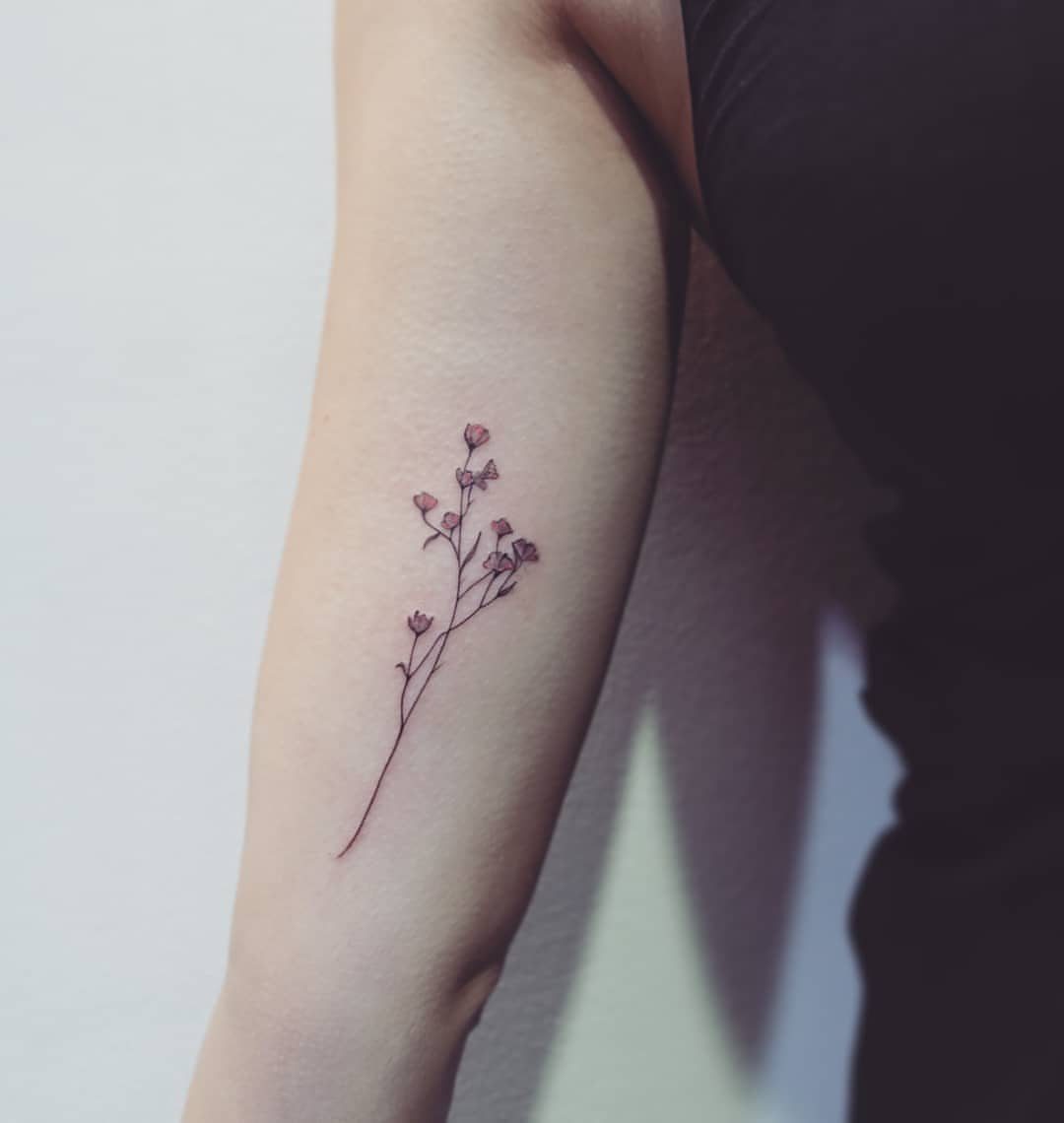 Small floral tattoo with pink blossoms on a person's inner upper arm