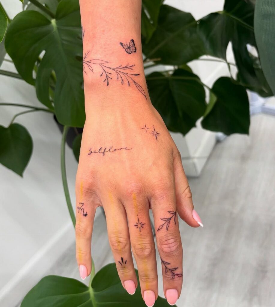 Hand and wrist with small black tattoos of plants, stars, and a butterfly.