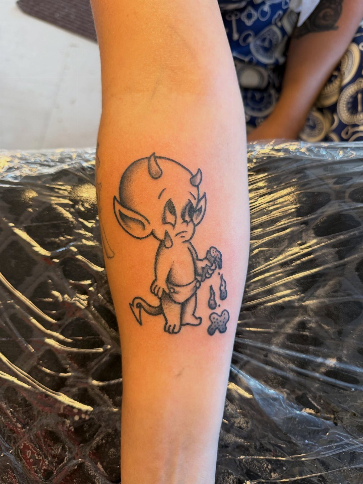 Small baby devil tattoo with a pitchfork on a person's forearm.