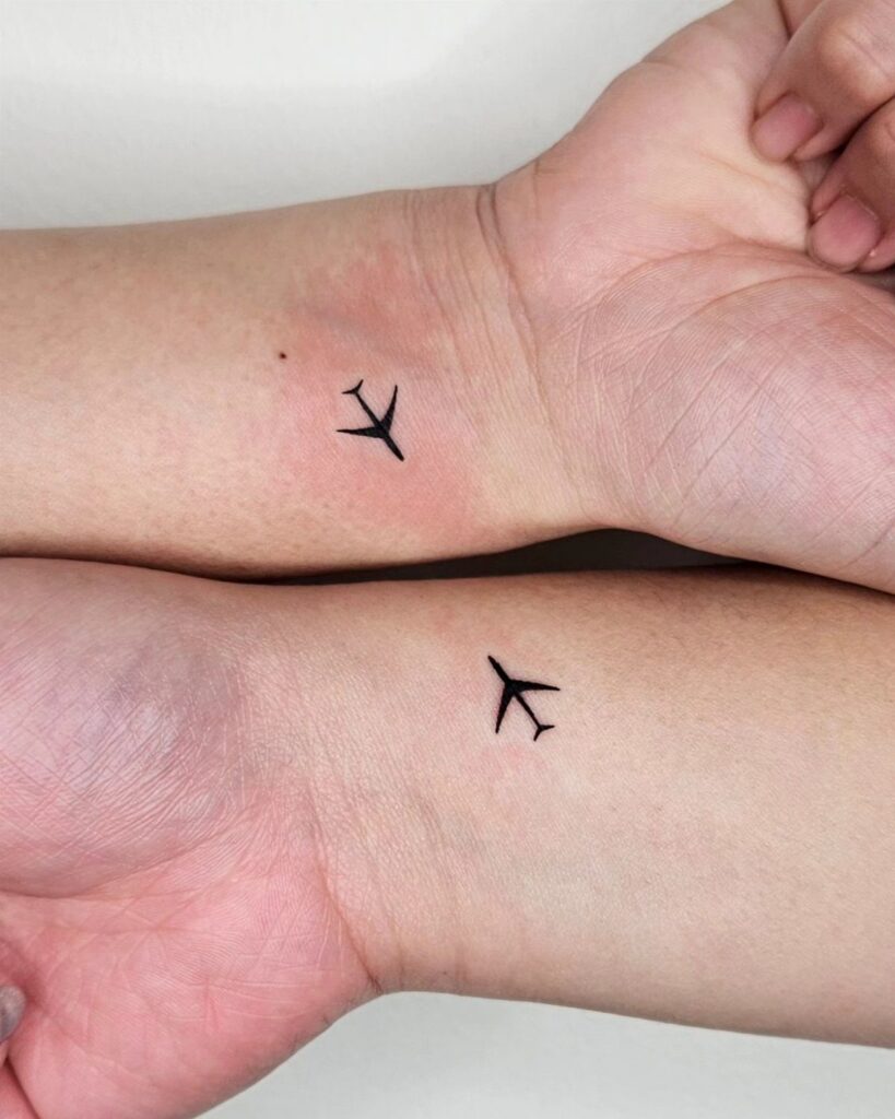 Two inner wrists with small, simple black airplane tattoos.