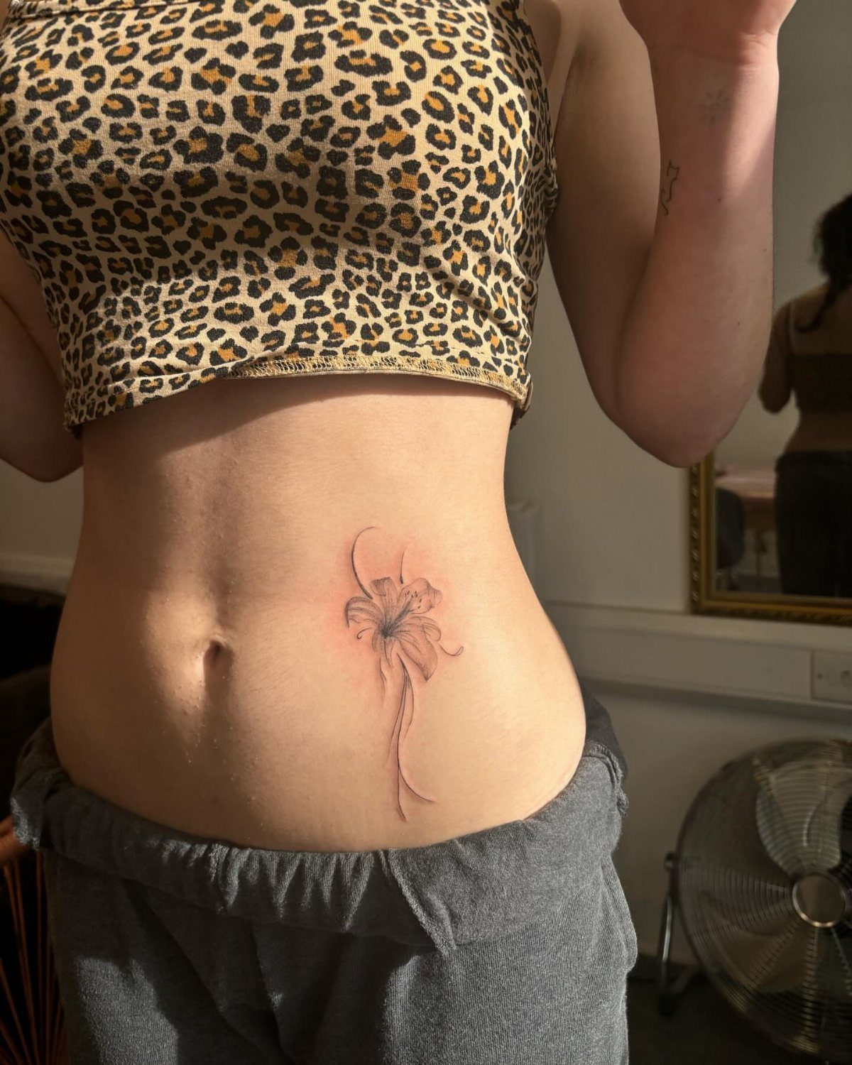 Woman's stomach with a red and black floral tattoo and leopard print top