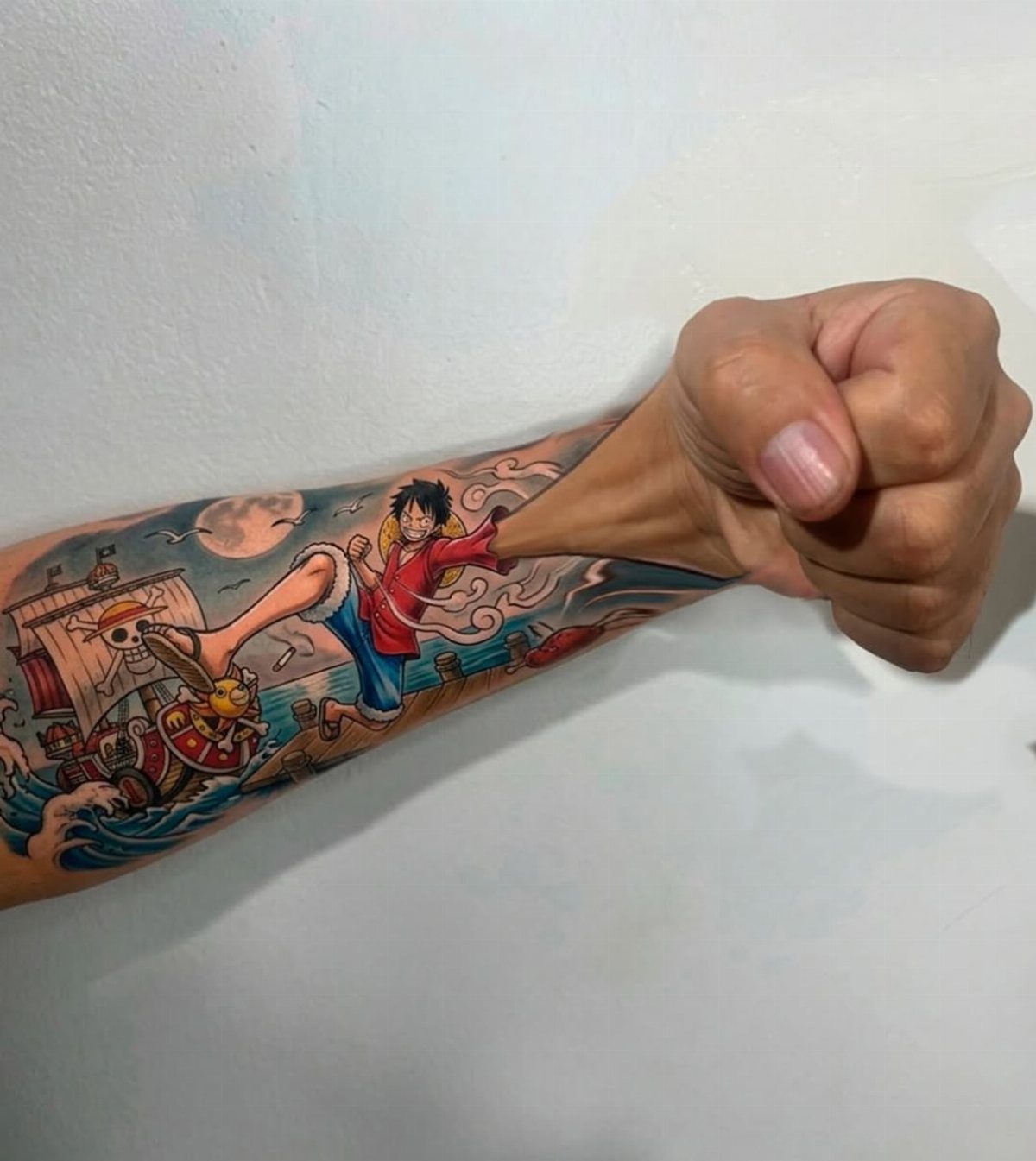 Colorful anime tattoo of Luffy on a man's forearm with a clenched fist.