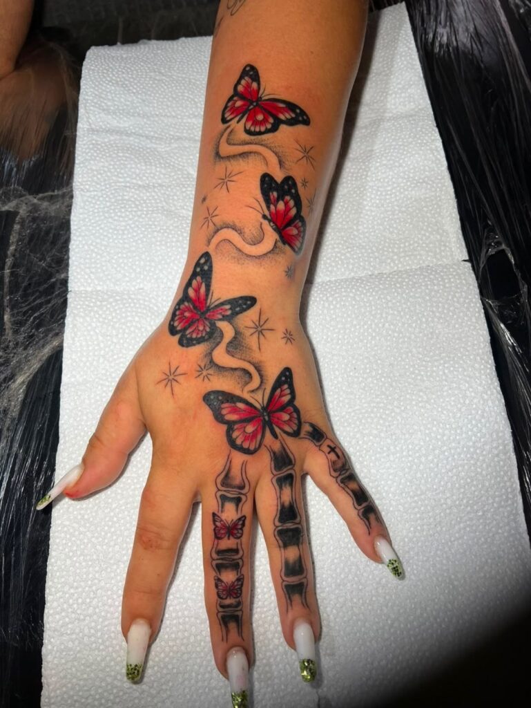 Hand and wrist with red butterfly tattoos and black skeletal finger bone tattoos.