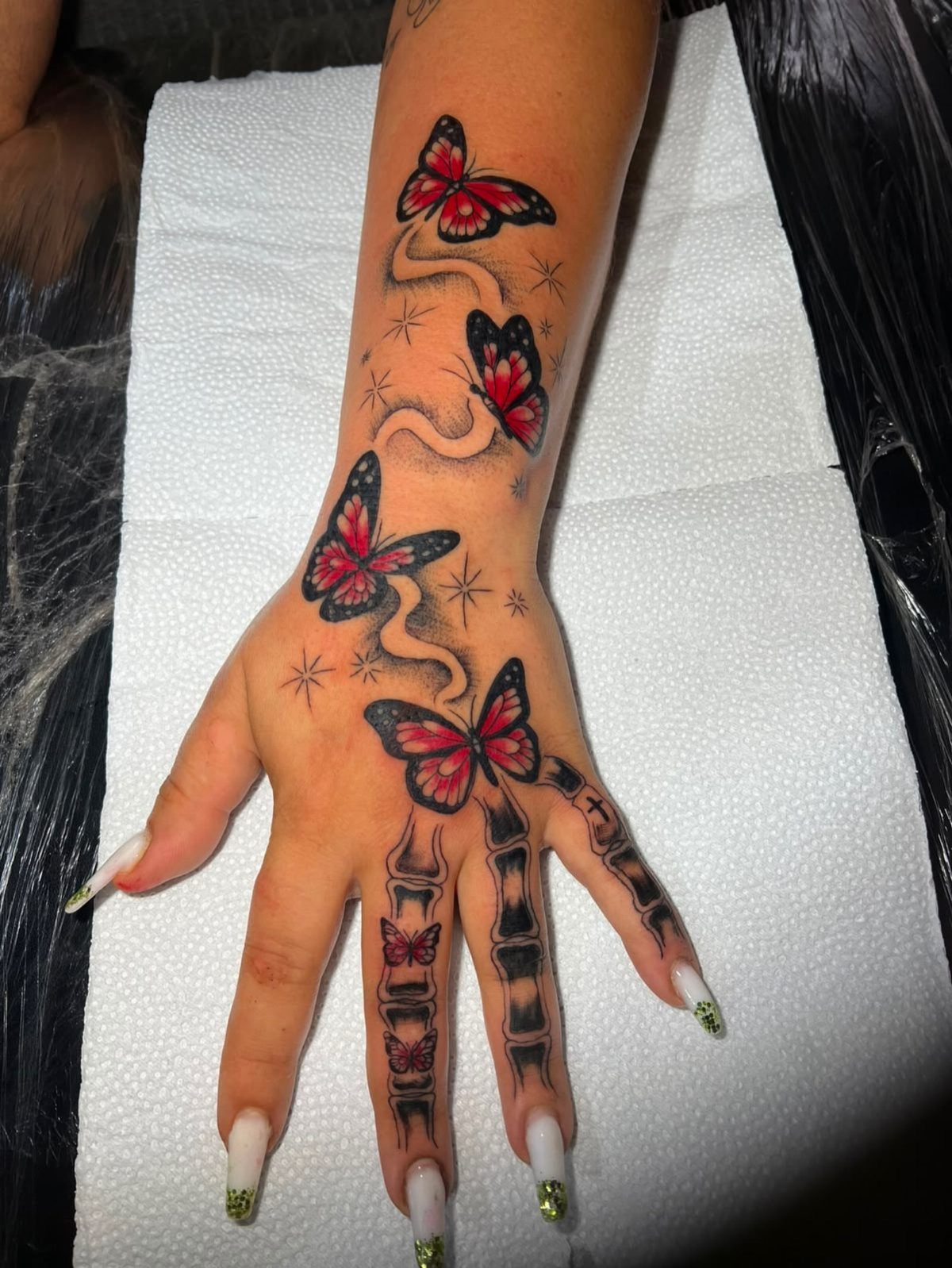 Hand and wrist with red butterfly tattoos and black skeletal finger bone tattoos.