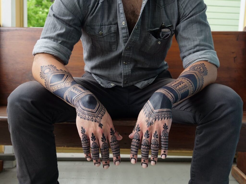 Man's hands and forearms covered in intricate black geometric and mandala tattoos.