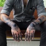 Man's hands and forearms covered in intricate black geometric and mandala tattoos.