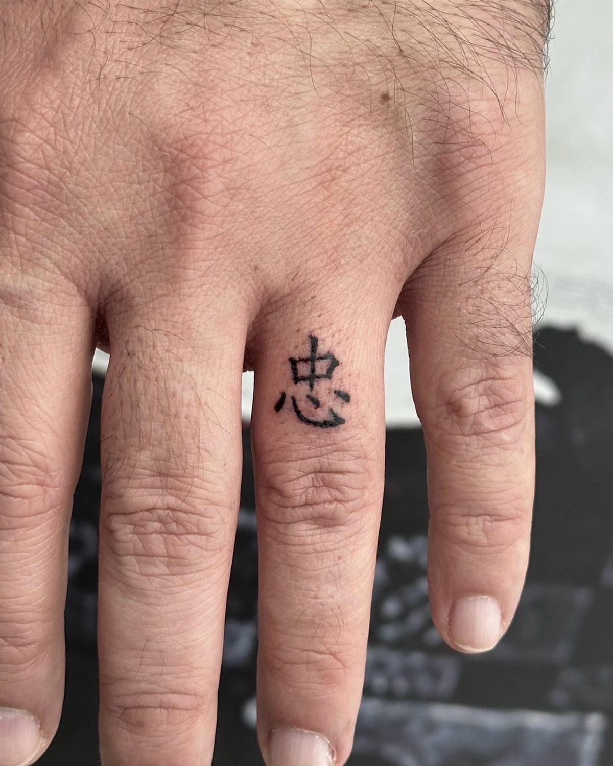 Small black Chinese character tattoo on the middle finger of a hand.