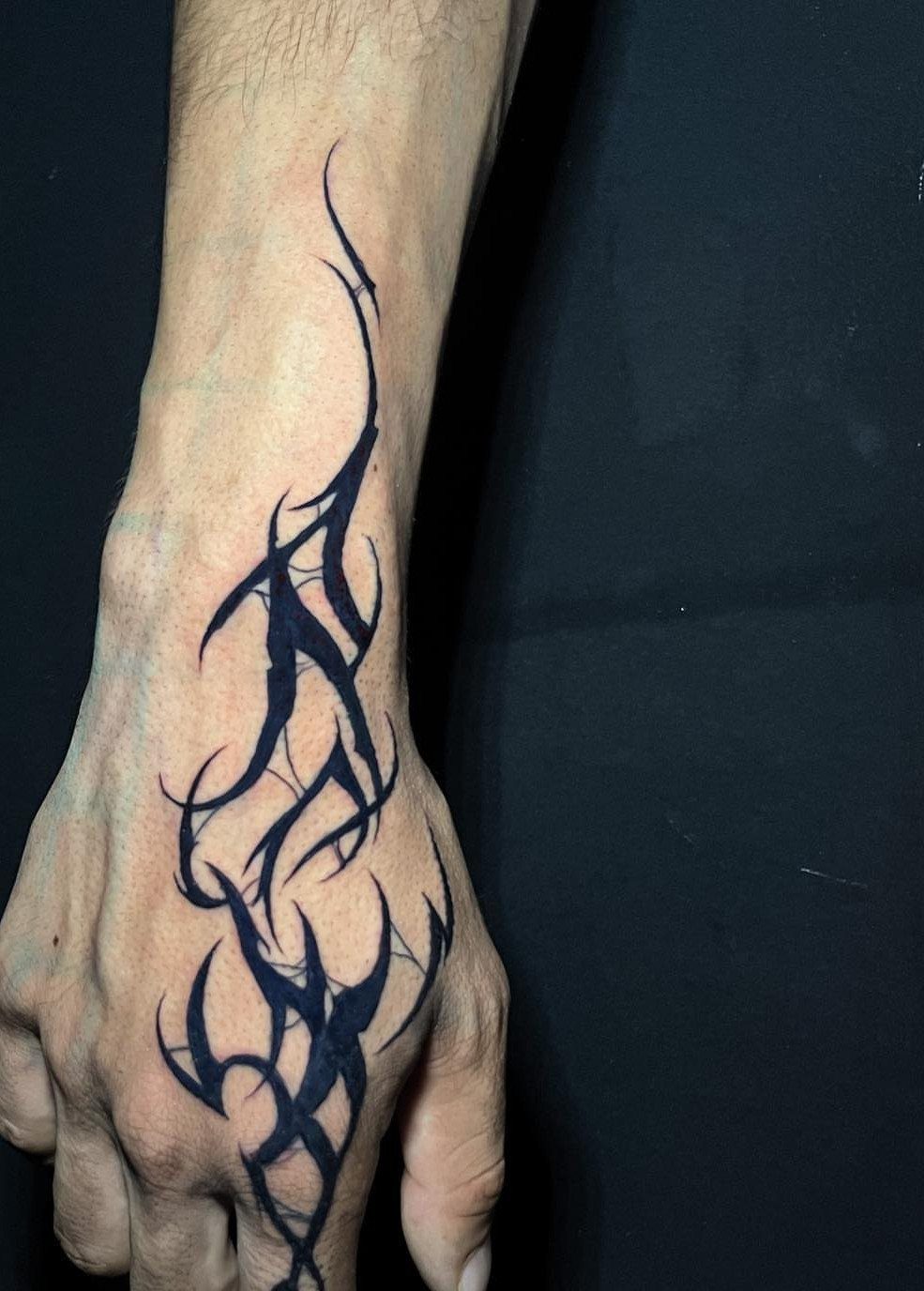 Man's hand and wrist with a black tribal tattoo on a dark background