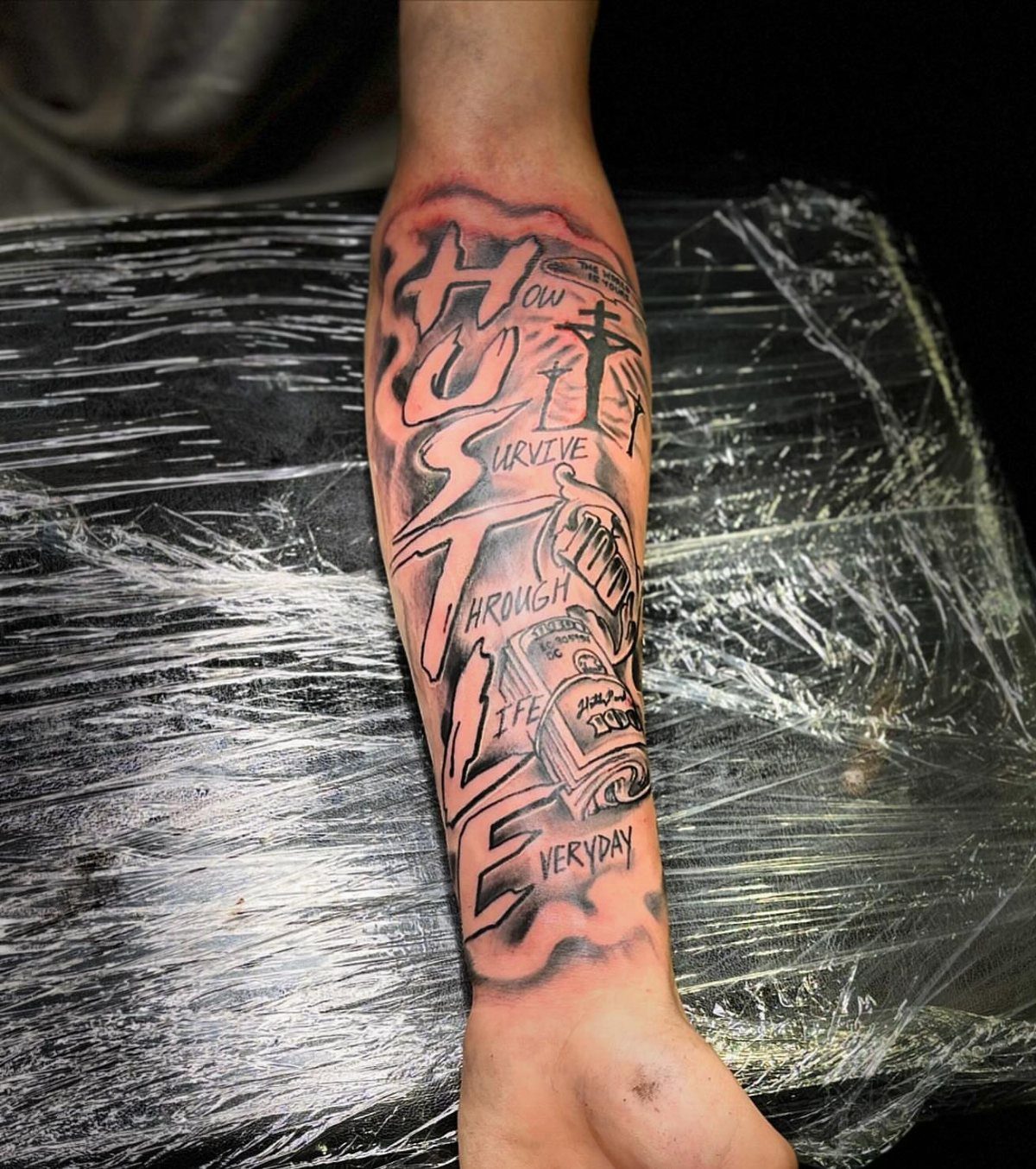 Lower arm with a detailed black and grey tattoo featuring the word HUSTLE.