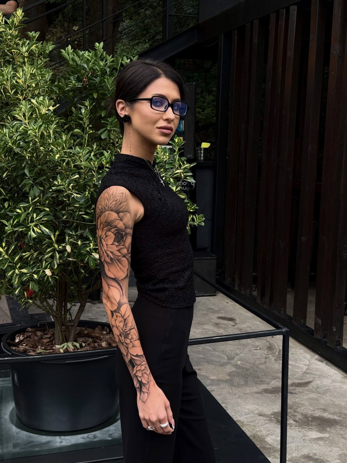 Woman with a full sleeve floral tattoo on her arm wearing black clothing.