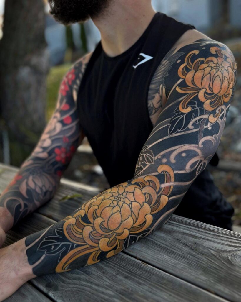Man with full tattoo sleeves featuring orange chrysanthemums and black ink patterns.