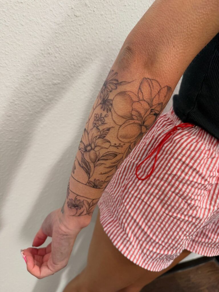 Floral black ink tattoo covering a person's arm from shoulder to wrist.